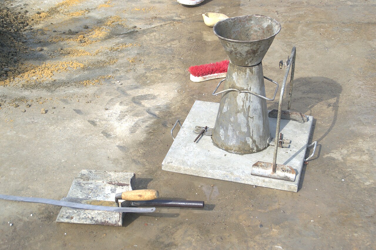 Laboratory concrete batching bench with fresh concrete mix, slump cone, tamping rod and scoop